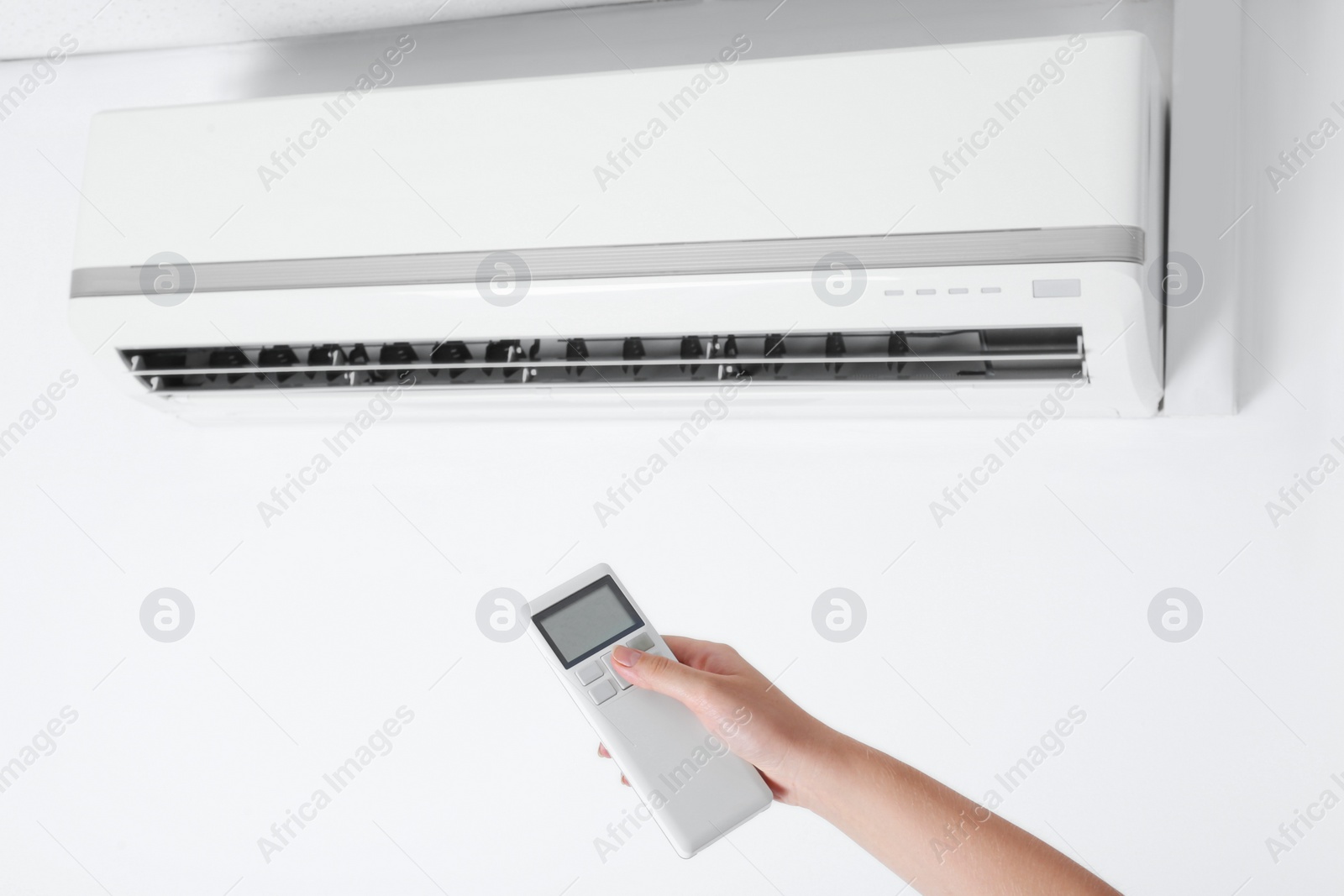 Photo of Woman operating air conditioner with remote control indoors, closeup