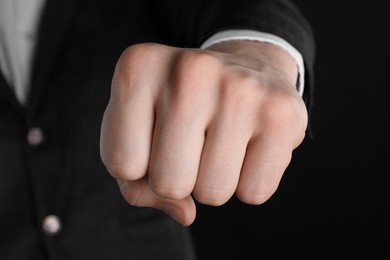 Businessman showing fist with space for tattoo on black background, closeup