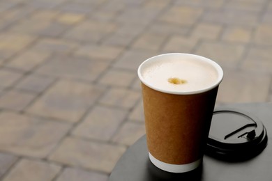 Photo of Cardboard cup with plastic lid on black table outdoors, space for text. Coffee to go