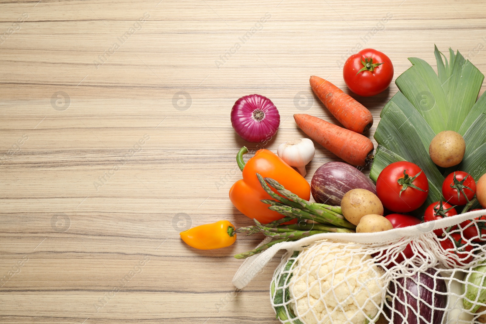 Photo of Fresh vegetables in eco mesh bag on wooden table, flat lay. Space for text