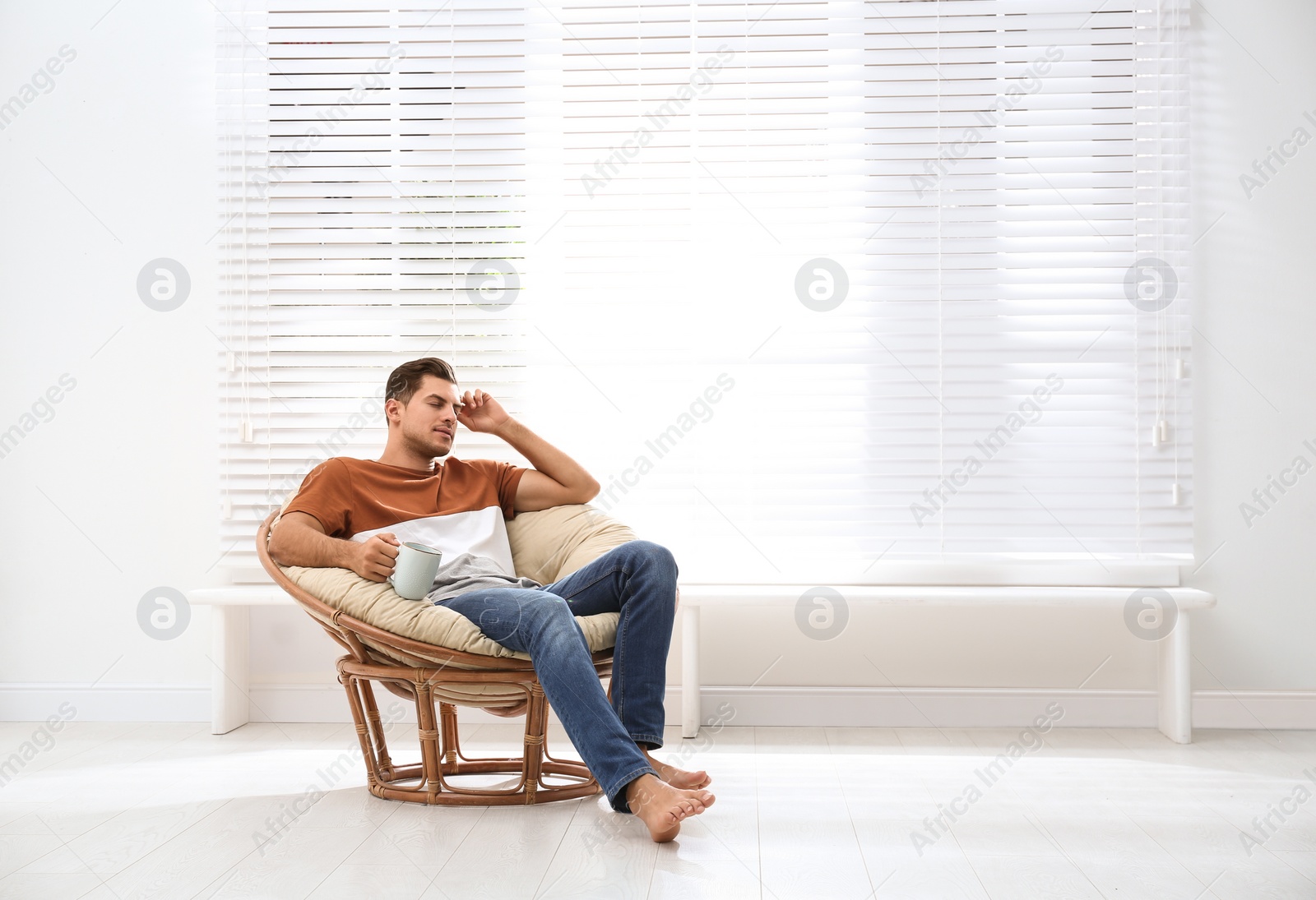 Photo of Attractive man relaxing in papasan chair near window at home. Space for text