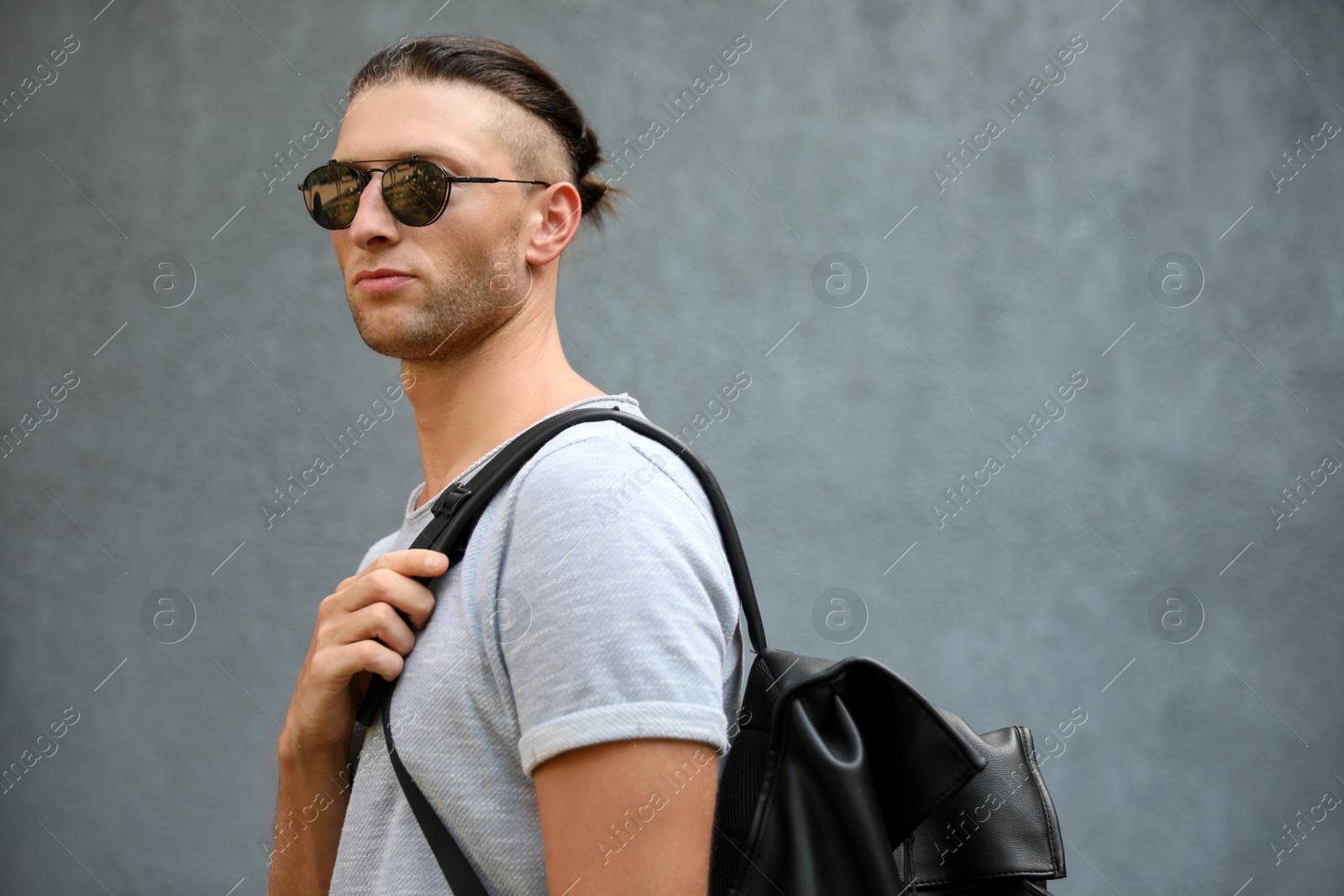 Photo of Handsome young man in stylish sunglasses with backpack near grey wall, space for text