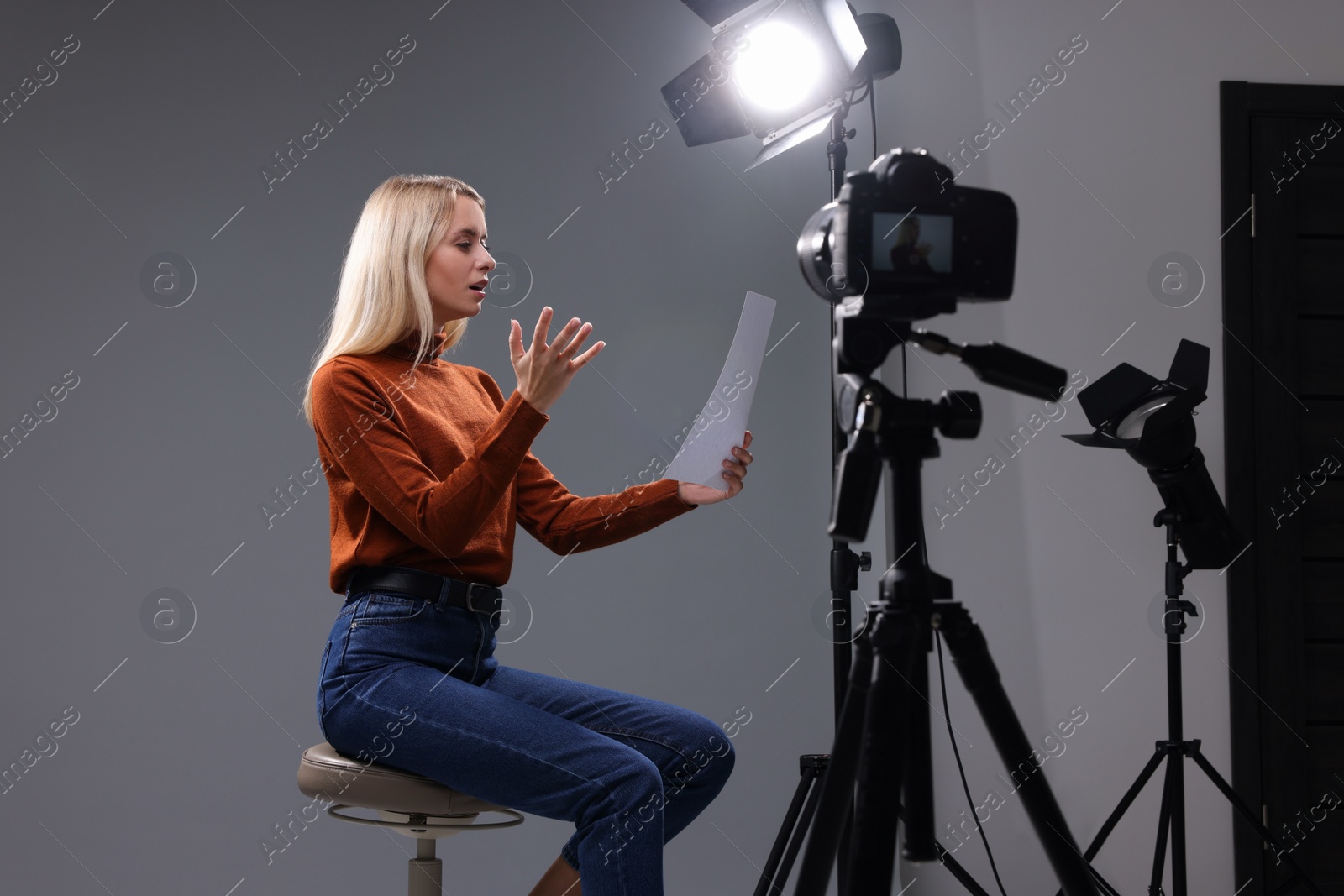 Photo of Casting call. Emotional woman with script sitting on chair and performing in front of camera in studio