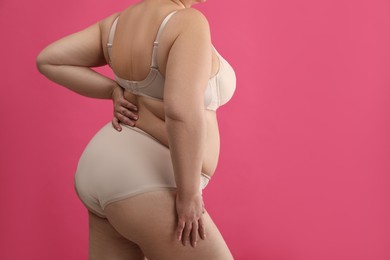 Photo of Overweight woman in beige underwear on pink background, closeup with space for text. Plus-size model