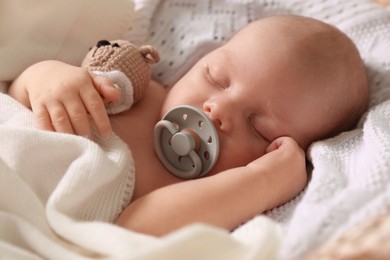 Cute newborn baby with pacifier sleeping on white blanket, closeup