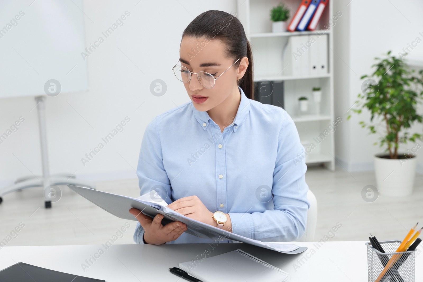 Photo of Young female intern with folder working at table in office