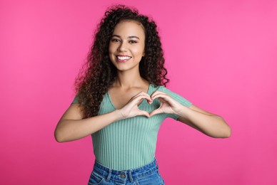 Photo of Happy young African-American woman making heart with hands on pink background