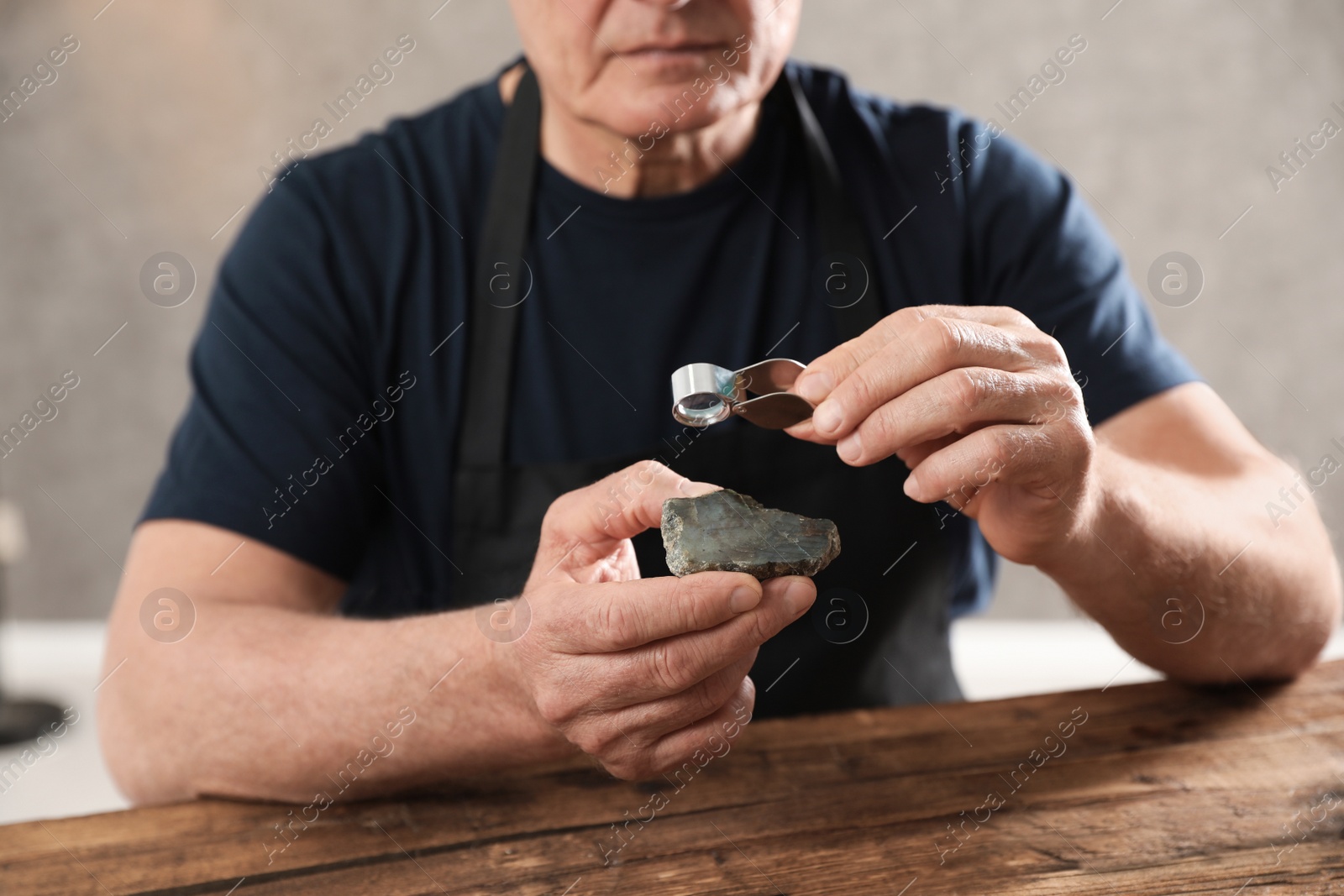 Photo of Male jeweler evaluating semi precious gemstone at table in workshop, closeup