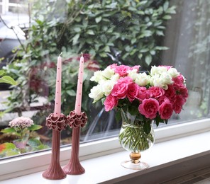 Vase with beautiful bouquet of roses and candles on windowsill indoors, space for text