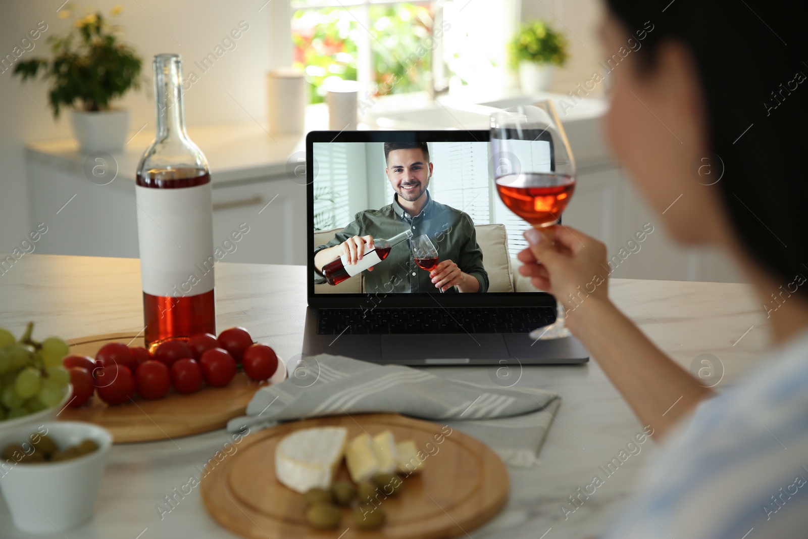 Photo of Friends drinking wine while communicating through online video conference in kitchen. Social distancing during coronavirus pandemic