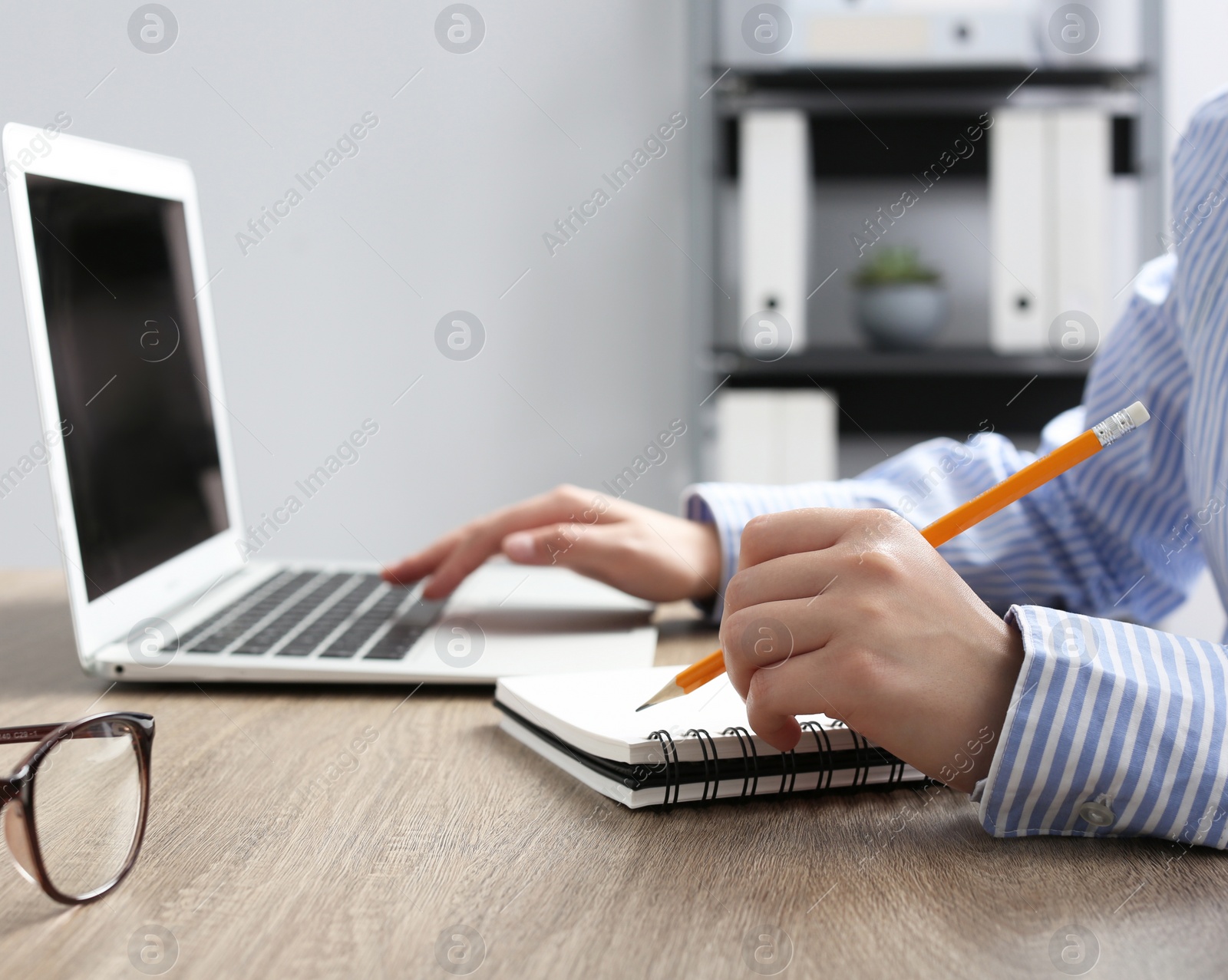 Photo of Woman with notebook working on laptop at wooden table in office, closeup