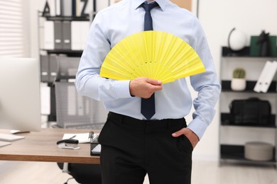 Photo of Businessman with yellow hand fan in office, closeup