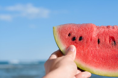 Photo of Child holding slice of fresh juicy watermelon near sea, closeup. Space for text