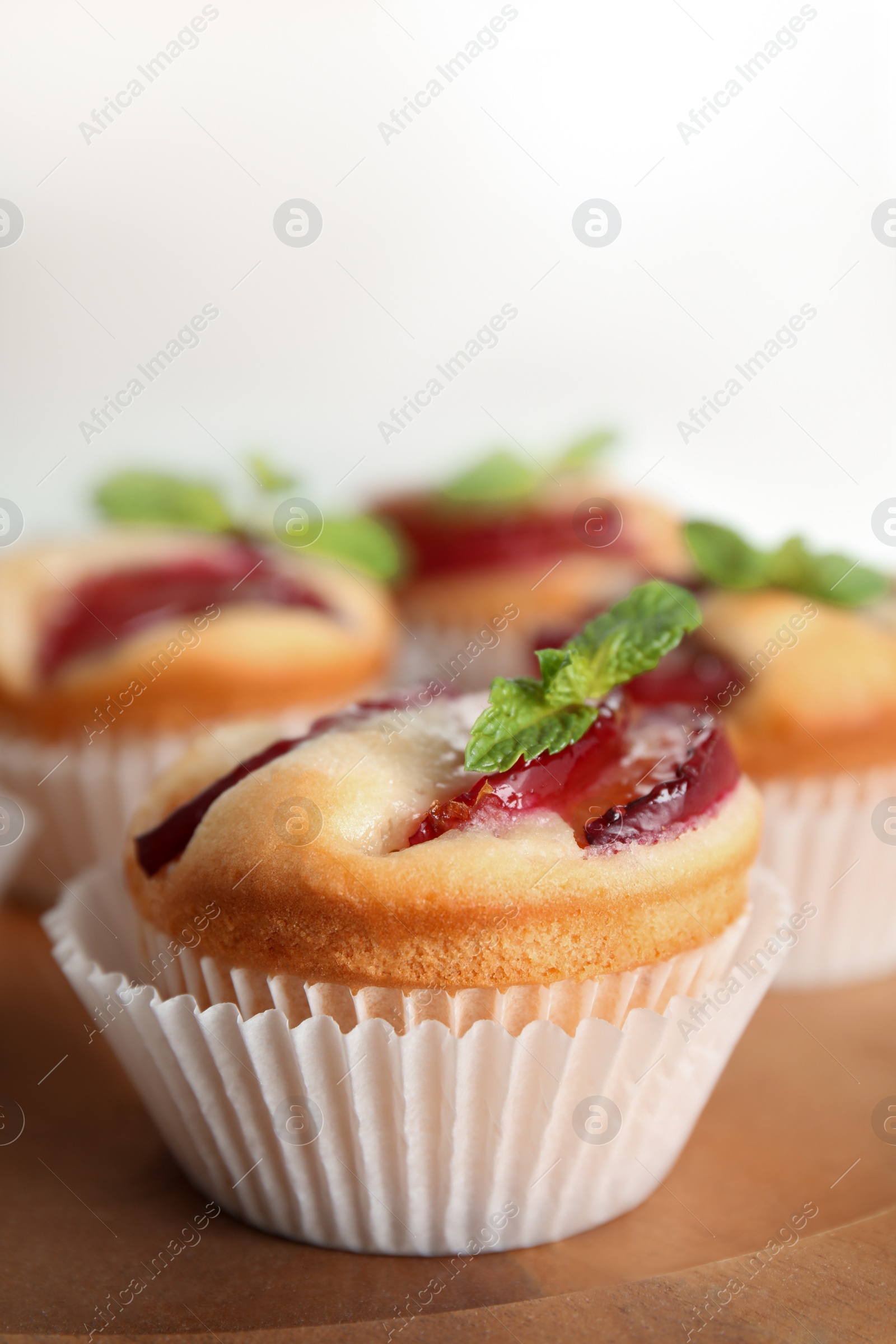 Photo of Delicious cupcakes with plums on wooden tray, closeup