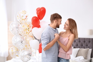 Photo of Young couple with air balloons in bedroom. Celebration of Saint Valentine's Day