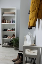 Photo of Shelving unit and shoe storage bench near white wall in hallway. Interior design