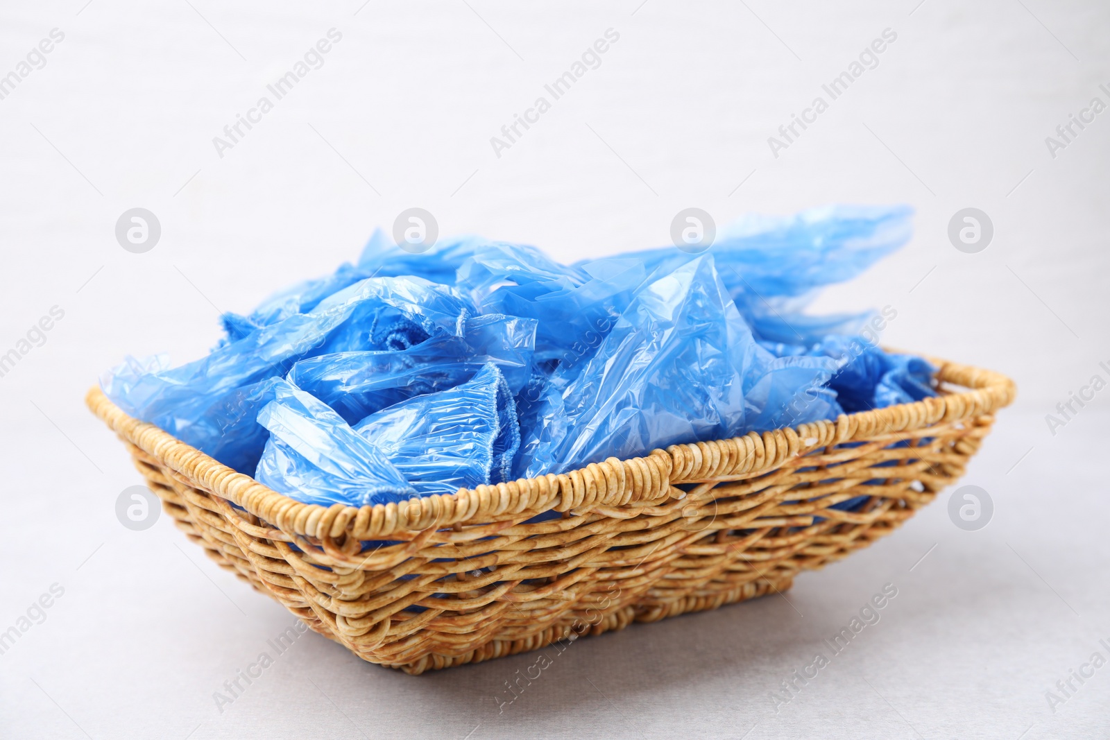Photo of Blue medical shoe covers in wicker basket on light background, closeup