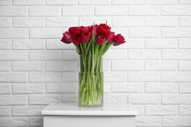 Photo of Bouquet of beautiful tulips in glass vase on white nightstand indoors