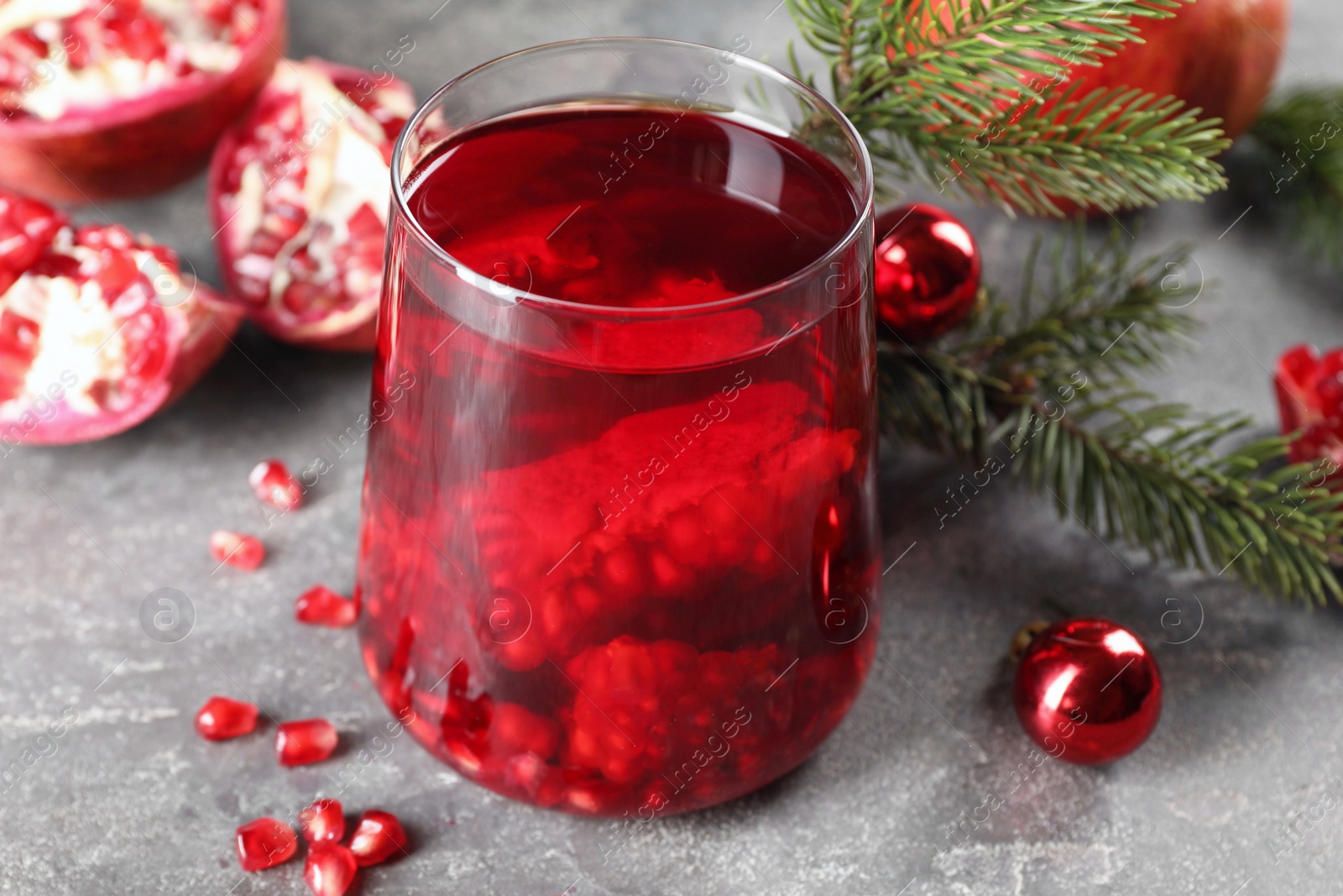 Photo of Aromatic Sangria drink in glass, Christmas decor and pomegranate grains on grey textured table, closeup