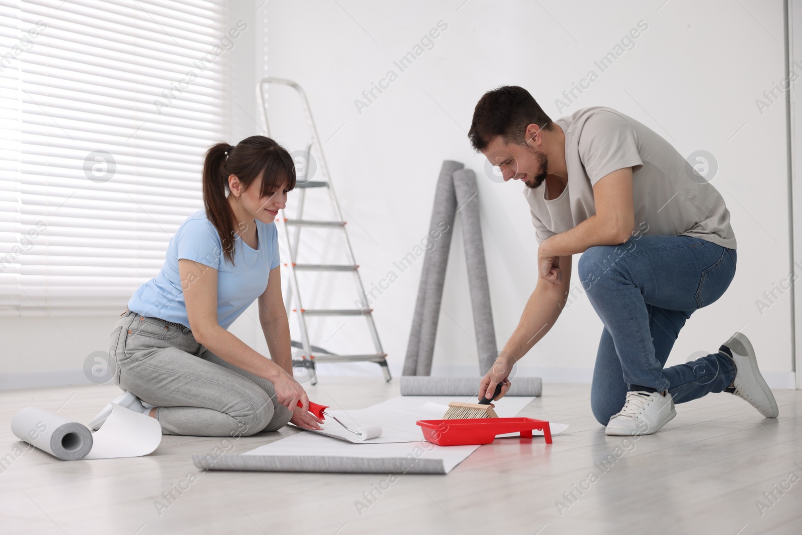 Photo of Couple applying glue onto wallpaper sheet in room