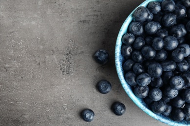 Photo of Bowl of tasty blueberries on grey table, top view with space for text
