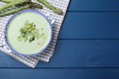 Photo of Delicious asparagus soup served on blue wooden table, flat lay. Space for text