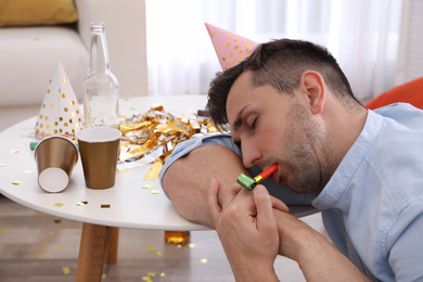 Photo of Young man in festive cap sleeping at table in room after party