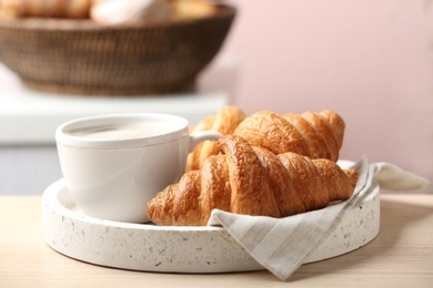 Photo of Plate of fresh croissants served with cup of coffee on wooden table indoors, closeup. French pastry