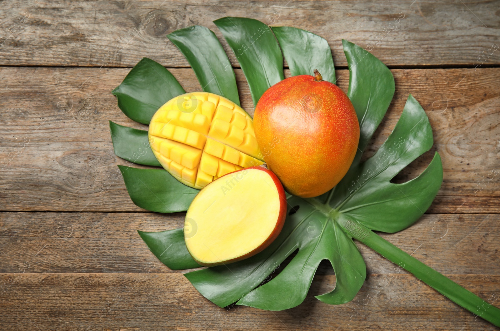 Photo of Flat lay composition with ripe mangoes and monstera leaf on wooden background