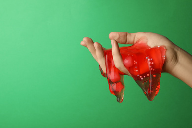 Woman playing with red slime on green background, closeup. Antistress toy