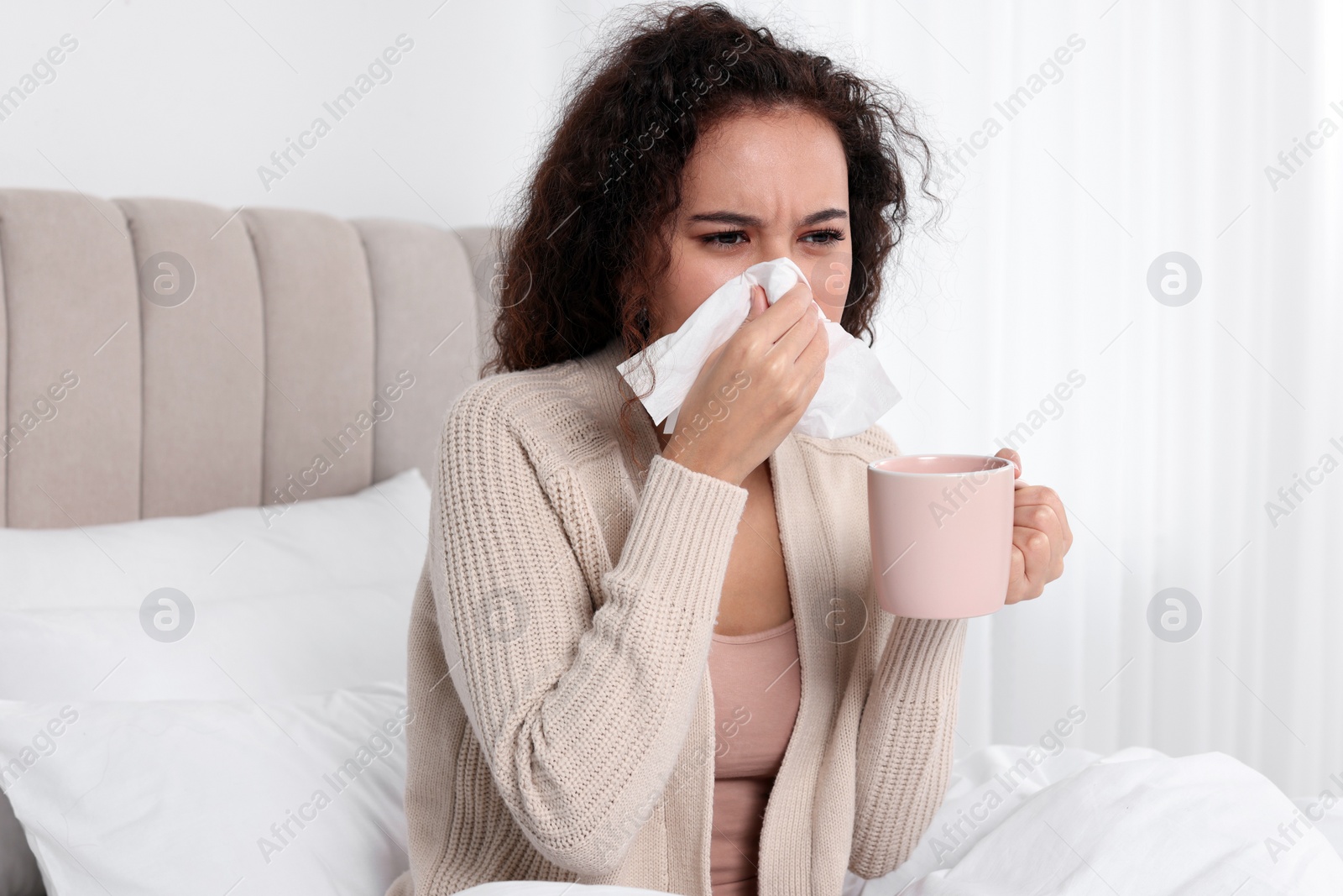 Photo of Sick African American woman with tissue and cup of drink in bed at home