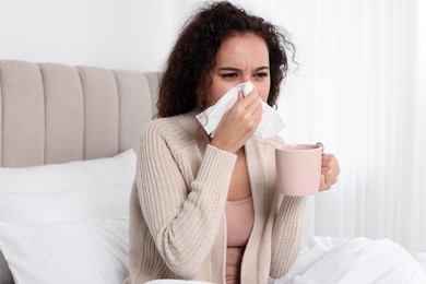 Sick African American woman with tissue and cup of drink in bed at home