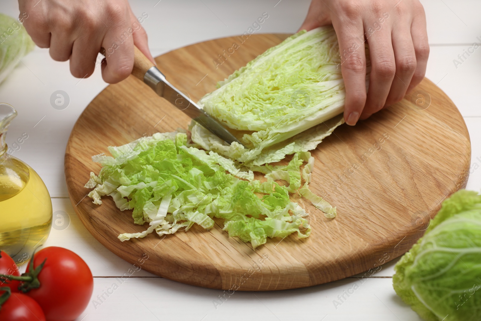 Photo of Woman cutting fresh chinese cabbage at white wooden table, closeup