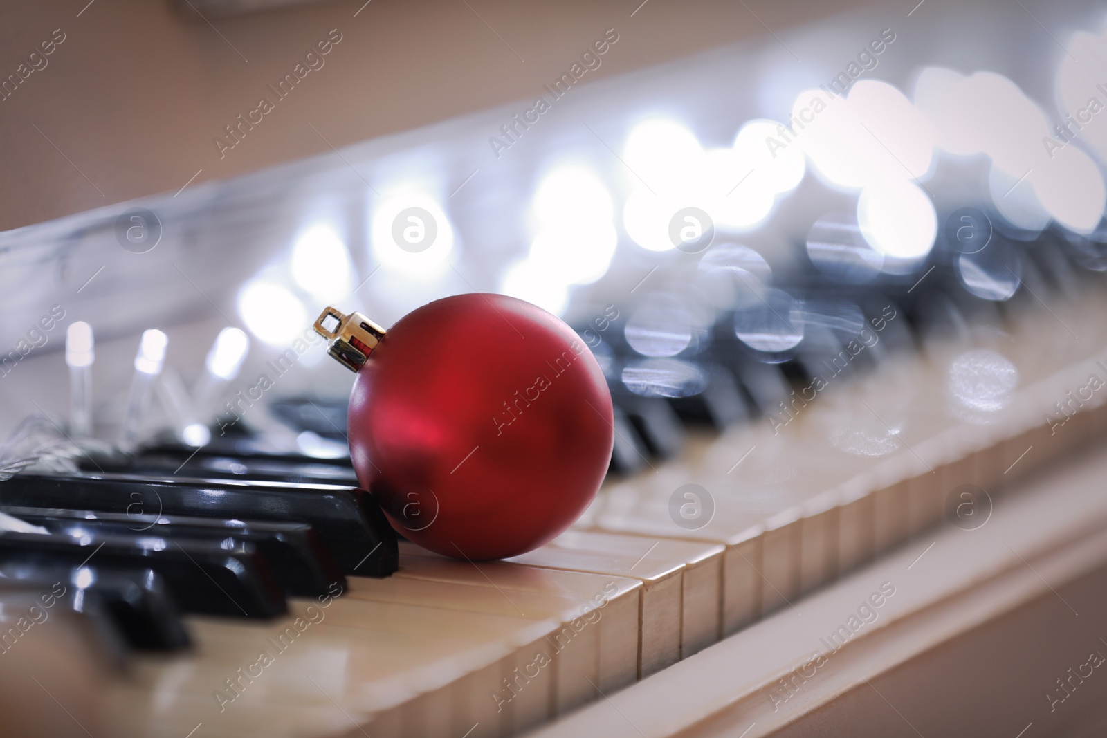 Photo of Beautiful red bauble and fairy lights on piano keys, closeup. Christmas music