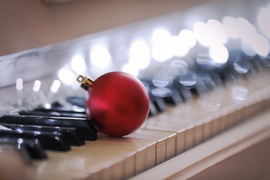Beautiful red bauble and fairy lights on piano keys, closeup. Christmas music