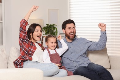 Photo of Excited family watching TV on sofa at home