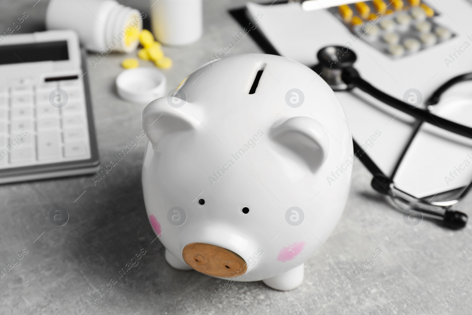 Photo of Piggy bank, stethoscope, calculator, clipboard and pills on light grey table, closeup. Medical insurance