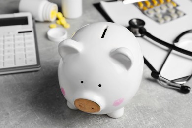 Photo of Piggy bank, stethoscope, calculator, clipboard and pills on light grey table, closeup. Medical insurance