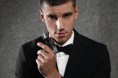 Photo of Handsome young man with bottle of perfume on grey stone background