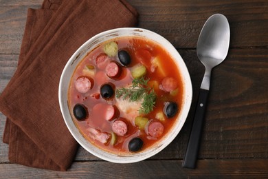 Photo of Meat solyanka soup with thin dry smoked sausages in bowl on wooden table, top view