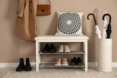 Photo of Stylish storage bench with different pairs of shoes near beige wall in hall
