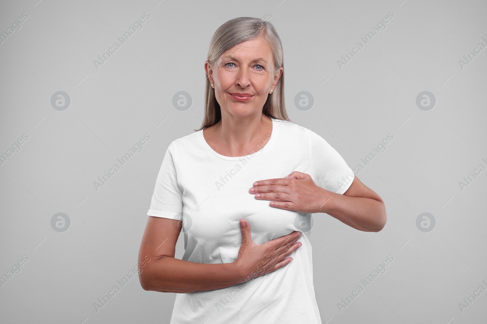 Photo of Beautiful senior woman doing breast self-examination on light grey background