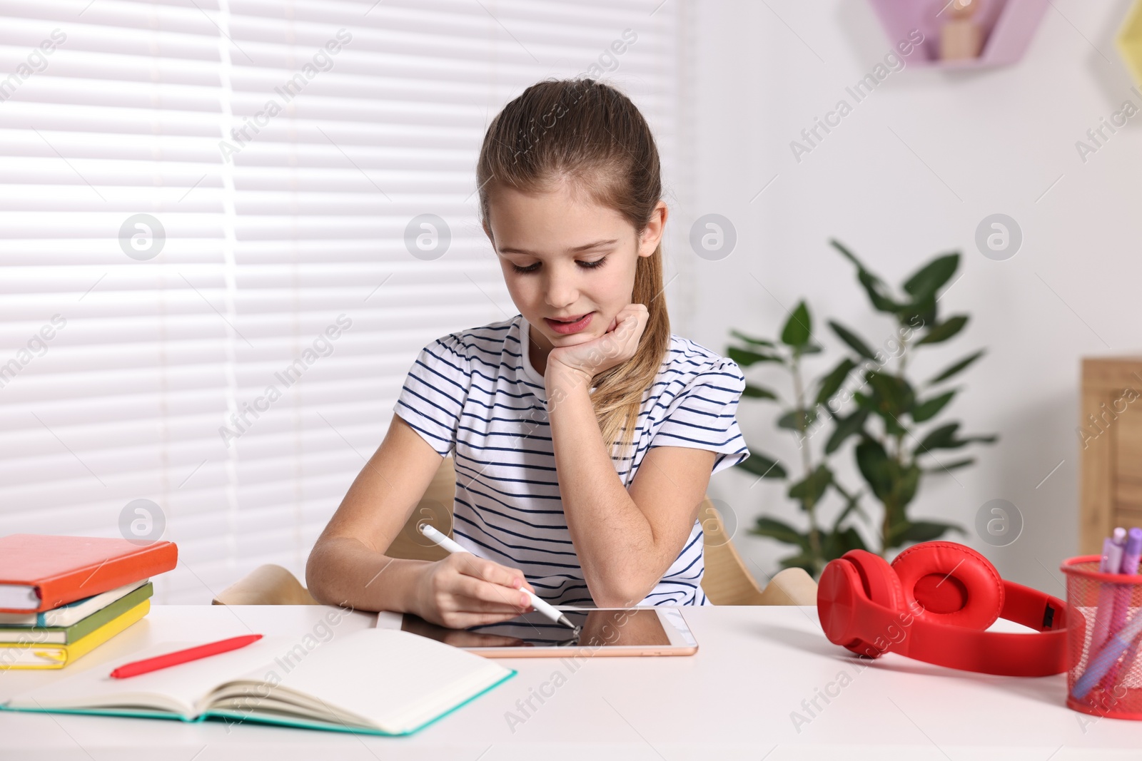 Photo of E-learning. Cute girl using tablet for studying online at table indoors