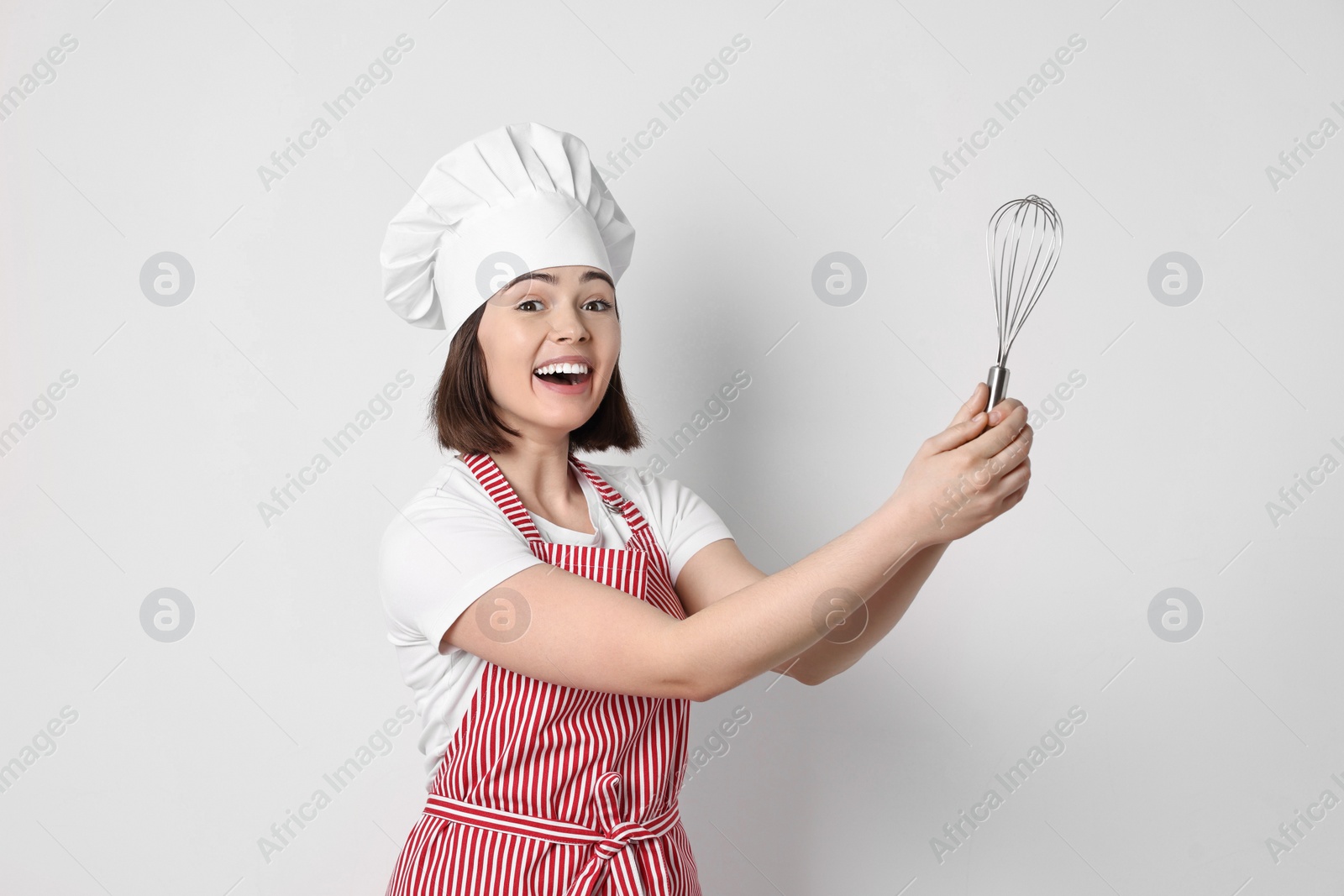 Photo of Happy confectioner holding whisk on light grey background