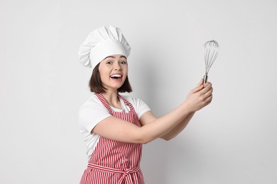 Photo of Happy confectioner holding whisk on light grey background