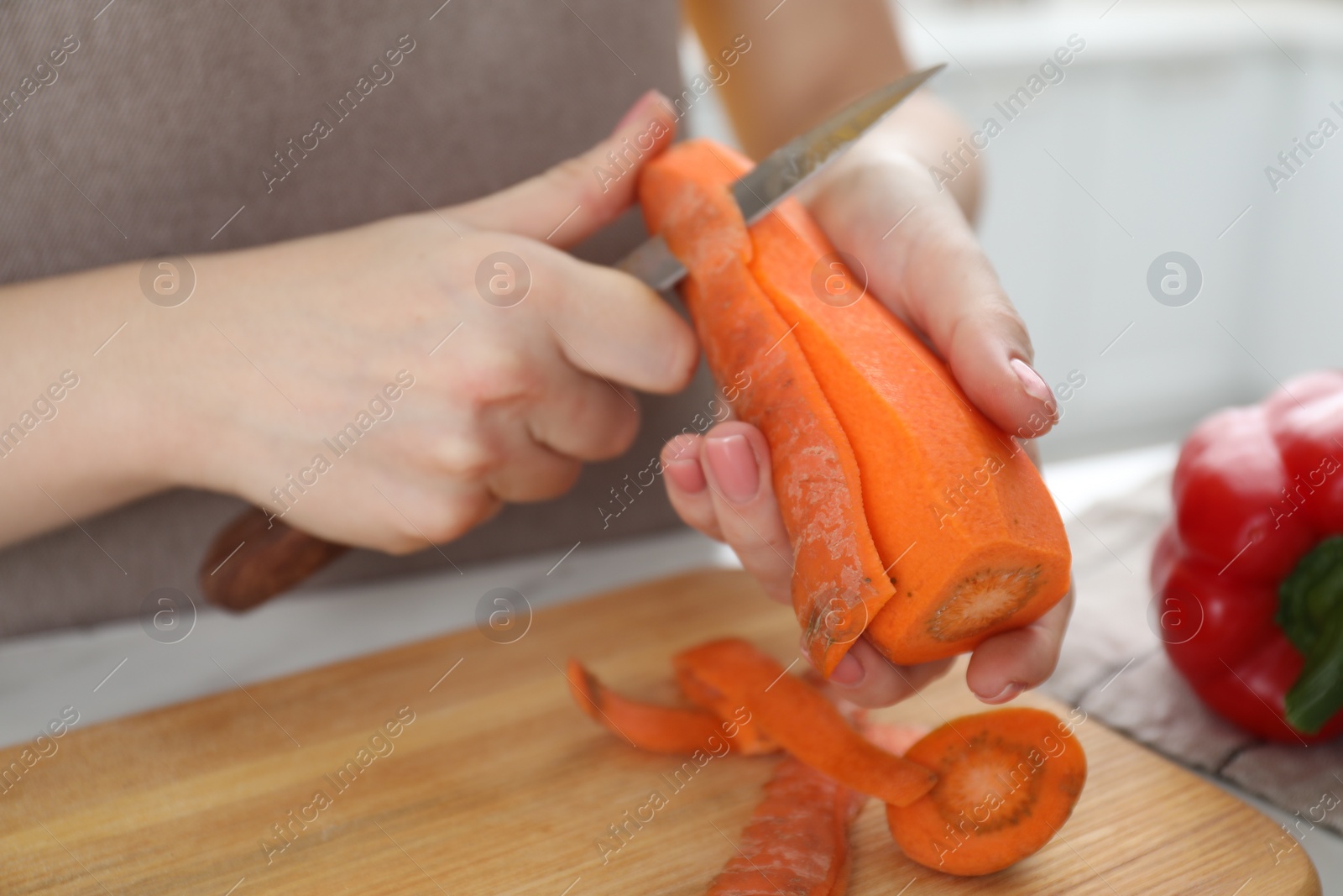 Photo of Woman peeling fresh carrot with knife at white table, closeup