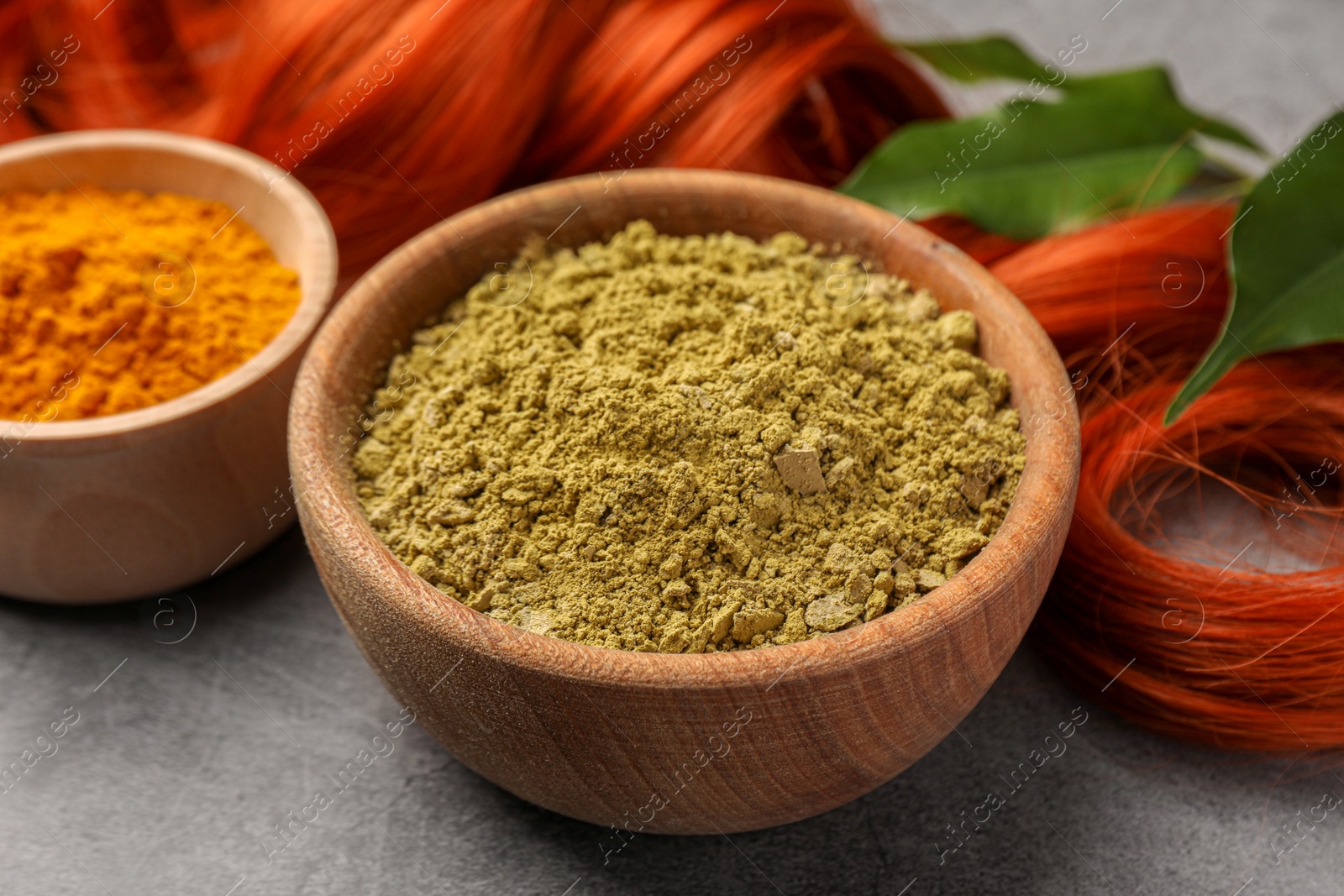 Photo of Henna, turmeric powder, red strand and green leaves on grey table, closeup. Natural hair coloring