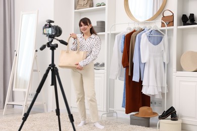 Smiling fashion blogger showing her bag while recording video at home