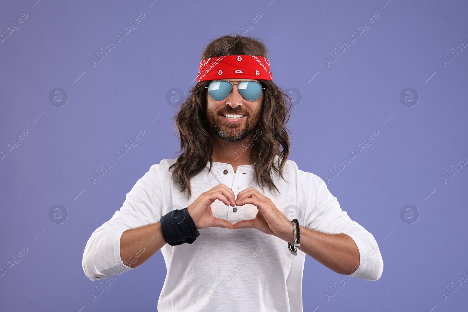Photo of Stylish hippie man making heart with hands on violet background