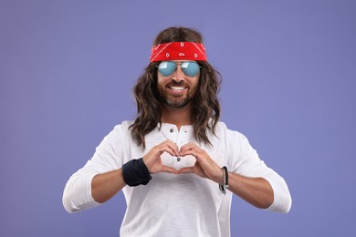 Photo of Stylish hippie man making heart with hands on violet background